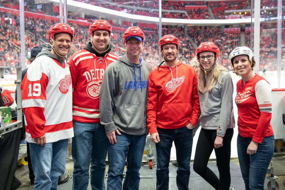 Six alumni smile for a photo together while getting prepared to get on the ice at the Detroit Red Wings GVSU Night